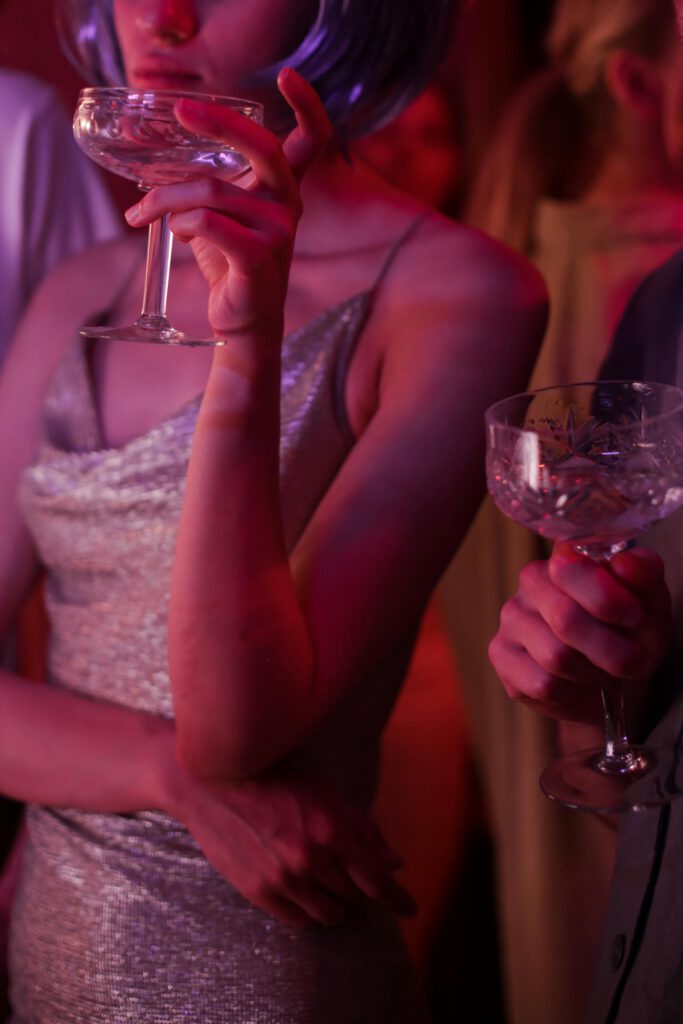 Fashionable party atmosphere with sparkling outfits and elegant drinks under neon lights.